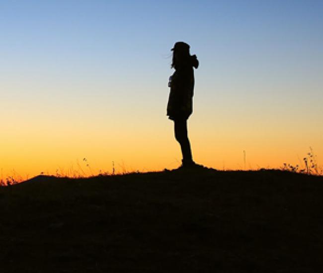 Silhouette of youth standing outside at sunset