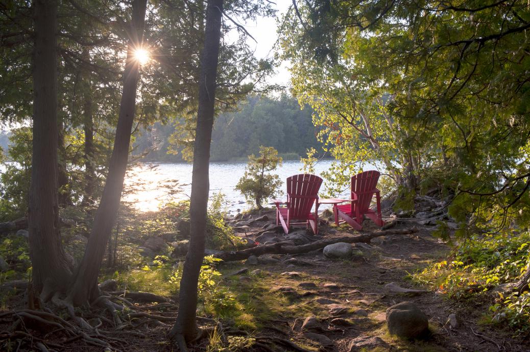 Peaceful setting in the woods with two empty chairs looking onto to lake