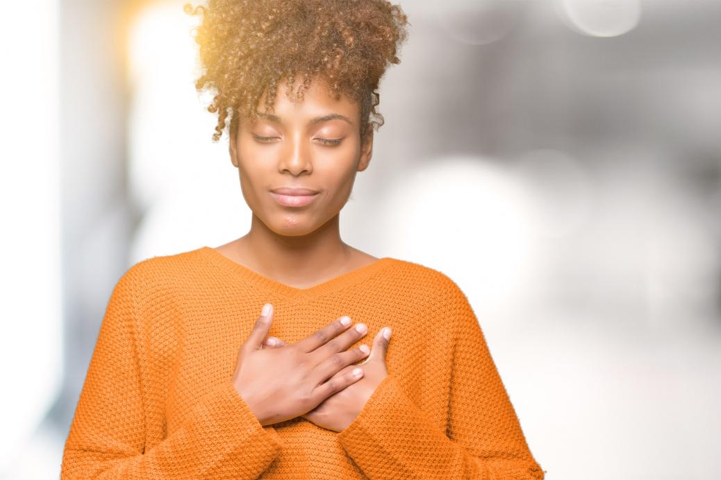 An African American woman smiling with hands on chest, closed eyes and grateful gesture on face