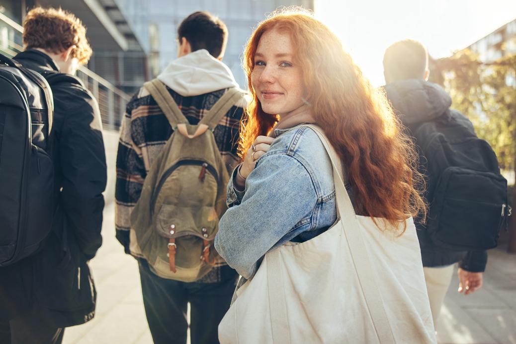 Female student walking in group and glancing back while going to class in college. 