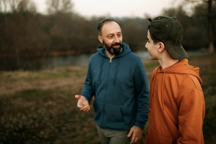 A man speaking with a teenager while walking in a park.