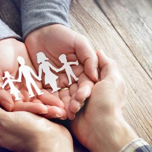 Pair of open hands holding onto a paper cut out of a family