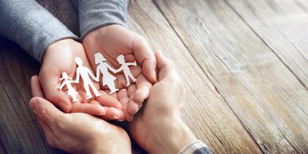 Pair of open hands holding onto a paper cut out of a family