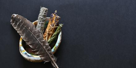 A feather with sweetgrass, sage, cedar, and tobacco in a shell