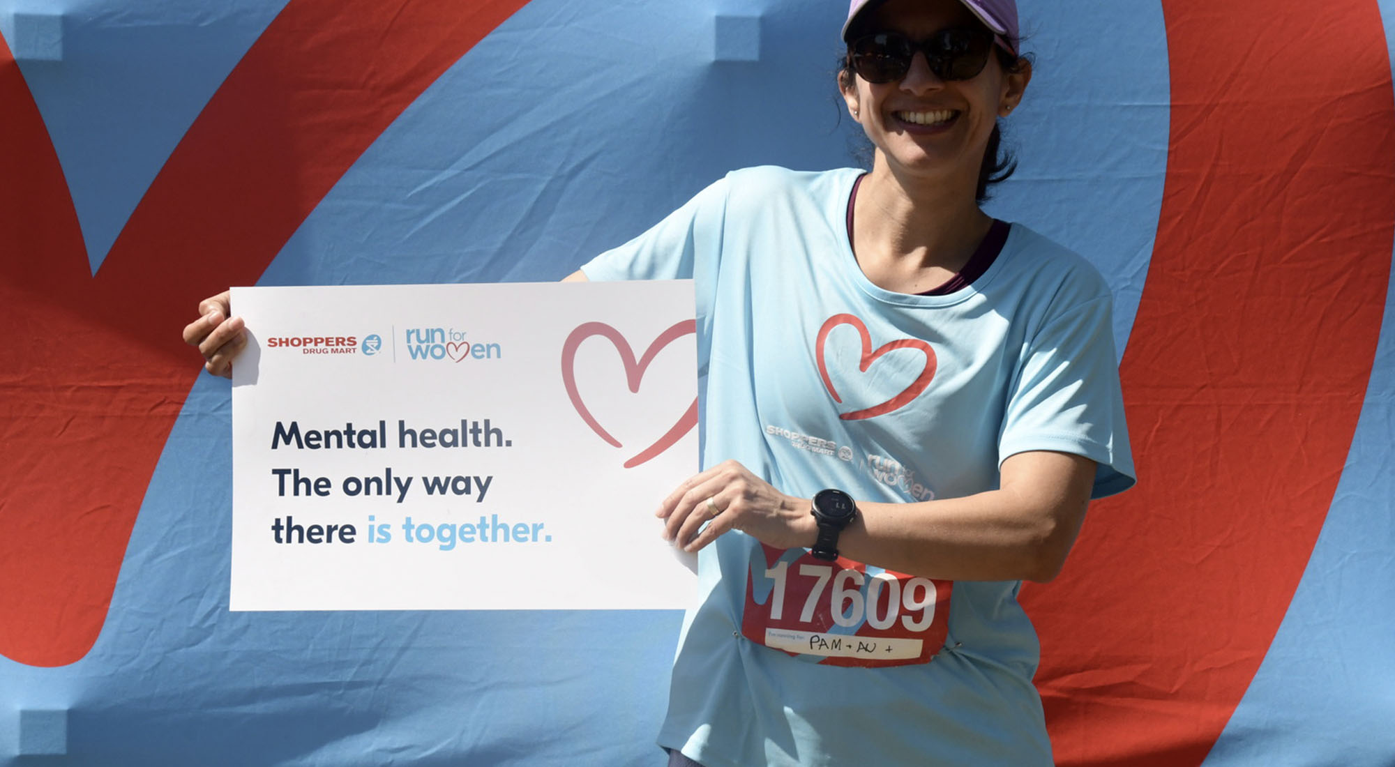 A woman holds a sign for Run for Women that reads: Mental health. The only way there is together.