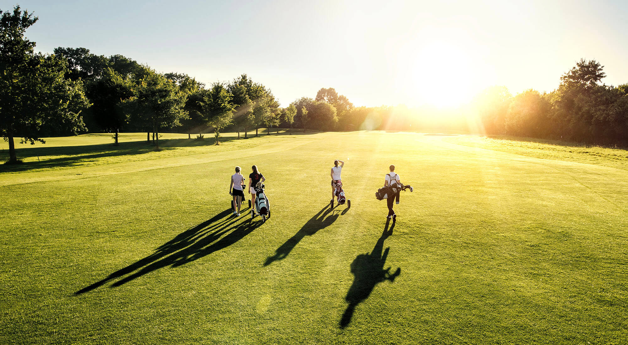 A group of golfers walk across the golf course on a bright, sunny day