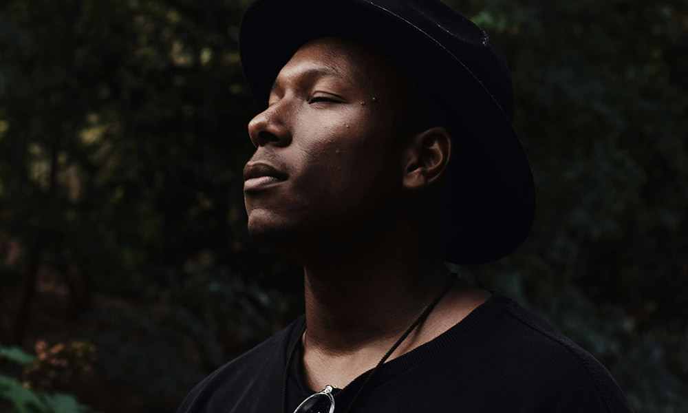 A man stands surrounded by greenery with his eyes closed