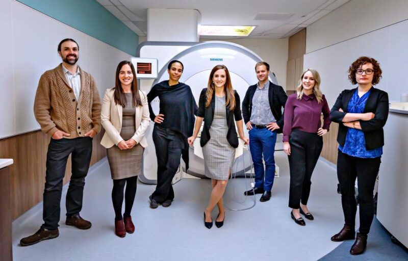 Group photo of the seven eRIMh team members standing in front of a brain imaging scanner.