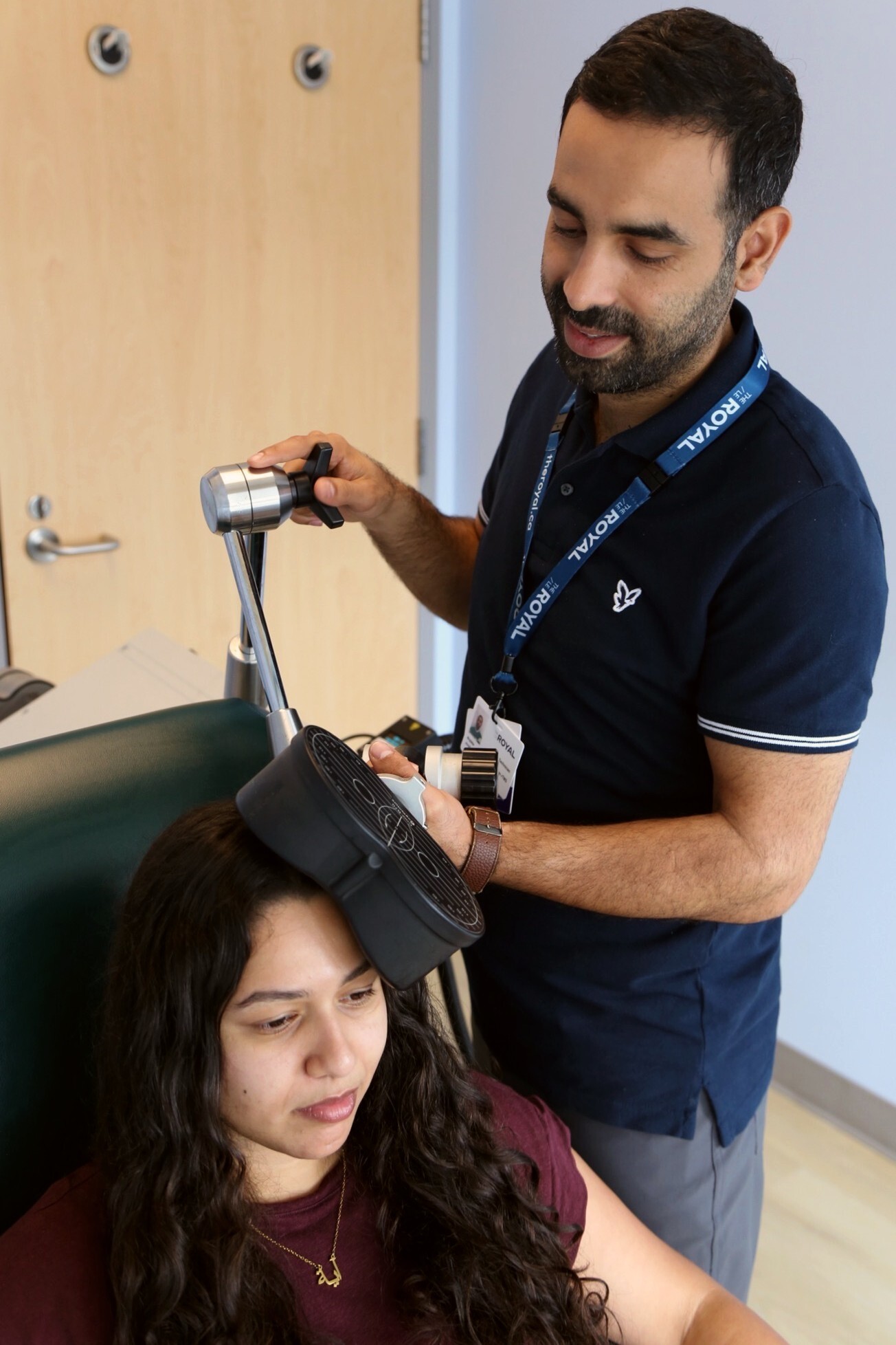 A clinician standing up using an electromagnetic coil on the scalp of a person sitting down